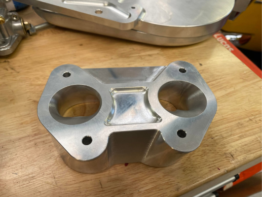 Finished CNC-machined metal adapter with two circular openings and fixing holes on a workshop bench