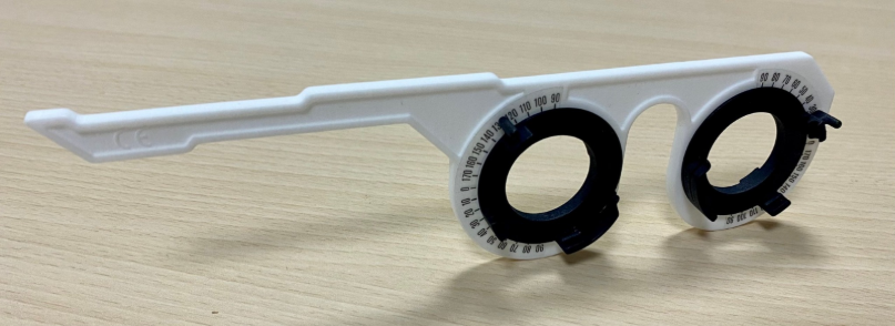 White ophthalmic lens testing device with a long handle, two black rotating lens holders and graduated scale stickers