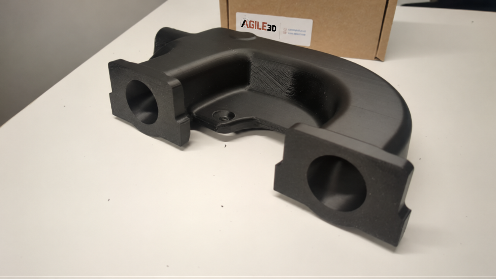 Black 3D-printed supercharger manifold prototype on a worktable